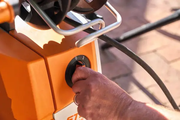 Hand dreht Schalter am orangefarbenen Hochdruckreiniger. Vorbereitung zum Anschluss an den Wasserhahn.